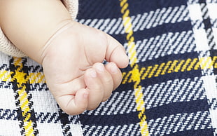 baby's left human hands on top of black and yellow plaid textile
